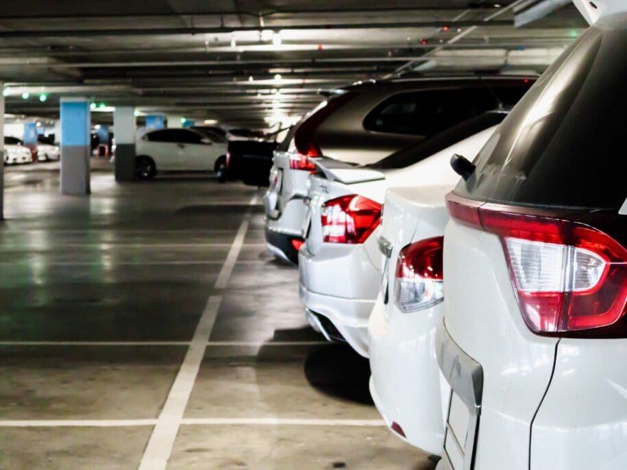 White cars parked in a concrete parking garage with support columns and fluorescent lighting