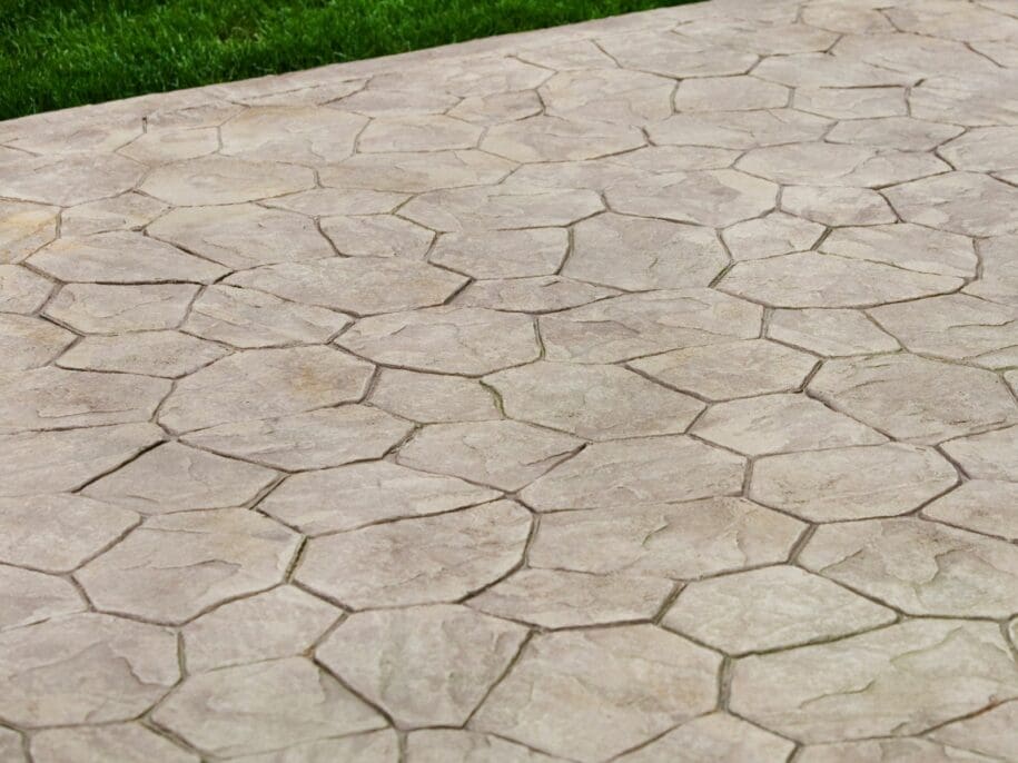 Close-up of a stone walkway featuring irregular polygonal pavers with natural veining and grout lines, adjacent to green grass
