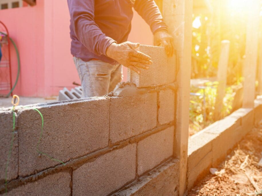 Worker in gloves laying concrete blocks during masonry unit replacement on a commercial building facade in bright sunlight
