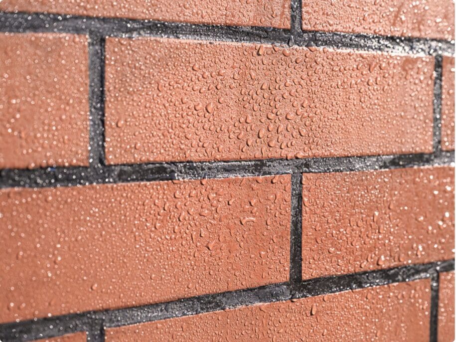Wet brick facade with dark mortar joints showing water beads on terracotta-colored bricks, demonstrating water-resistant coating application for masonry protection