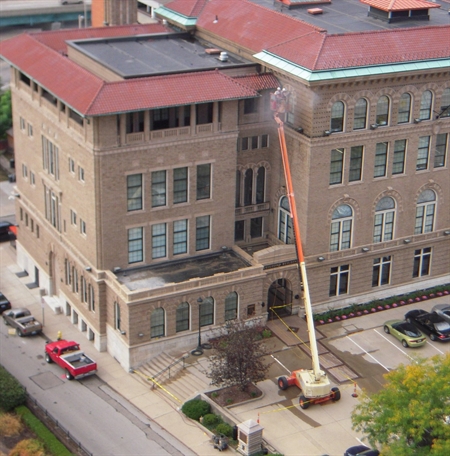 Aerial view of Cincinnati brick building with red roof undergoing commercial facade repair using construction crane and equipment