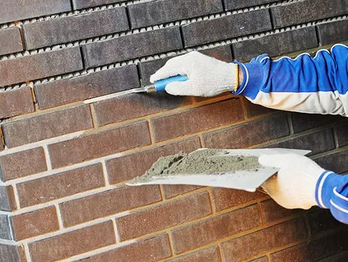 Worker applying mortar between bricks during tuckpointing masonry repair on commercial building facade
