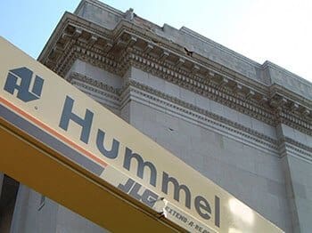 Historic brick building facade with ornate stone detailing above yellow Hummel storefront signage, showing masonry restoration and facade repair needs in Cincinnati